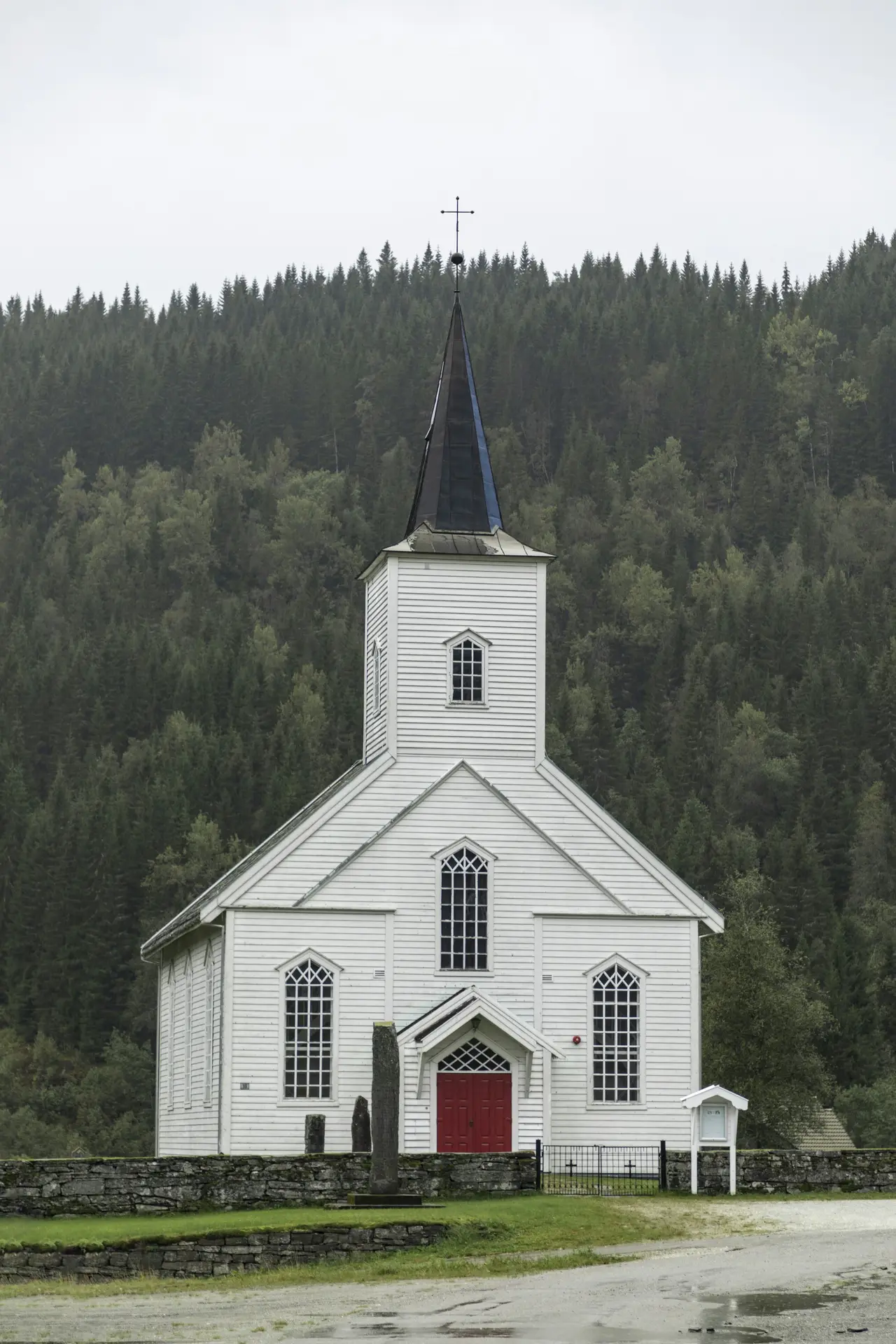 A white chapel with a tall steeple among evergreen trees