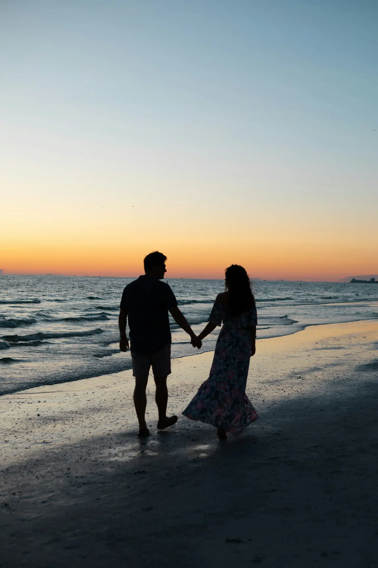 A couple holding hands as they walk along the beach at sunset